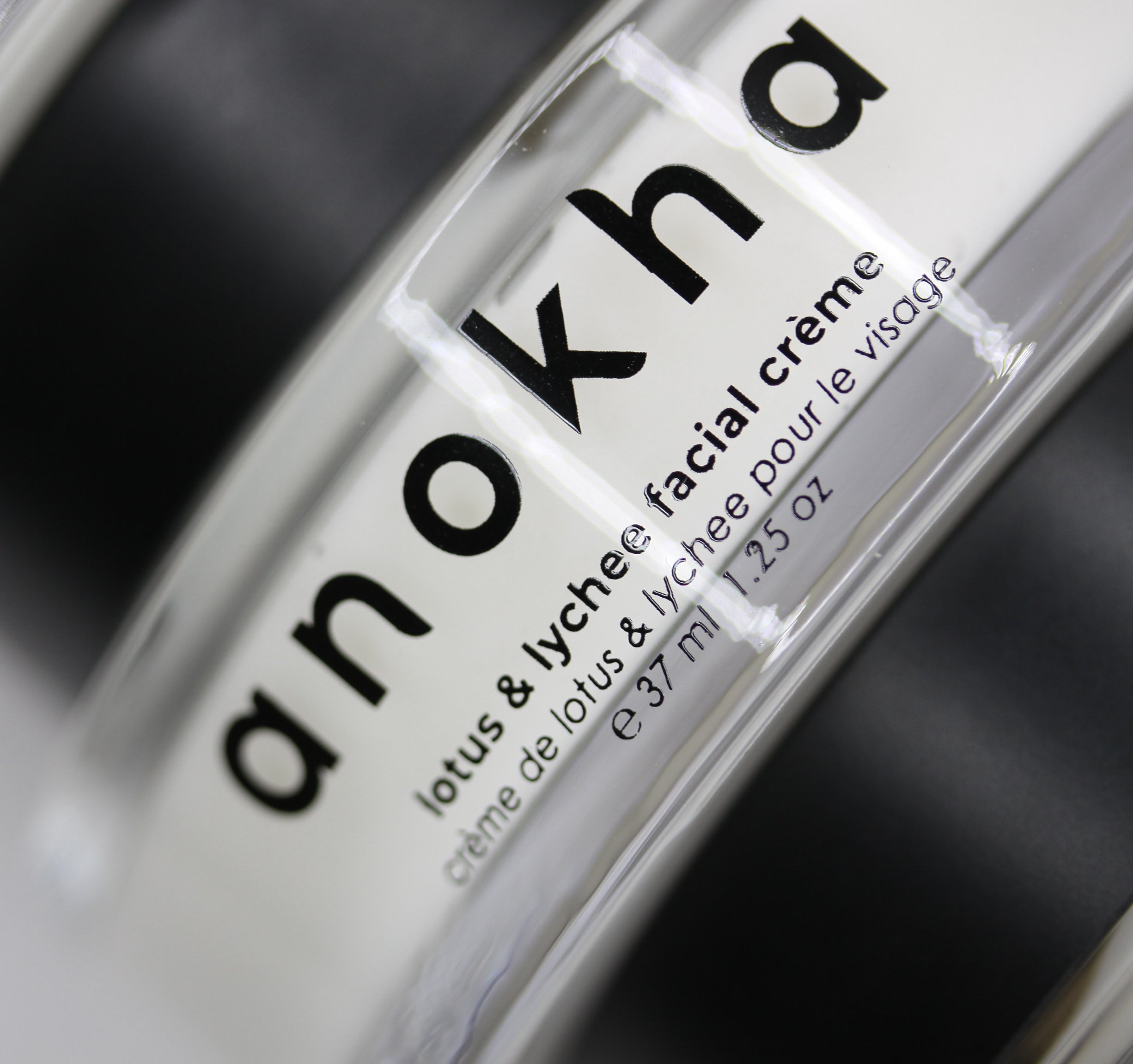 Close-up of a clear cosmetic bottle with a white label reading 'anokha lotus & lychee facial creme' on a dark background.