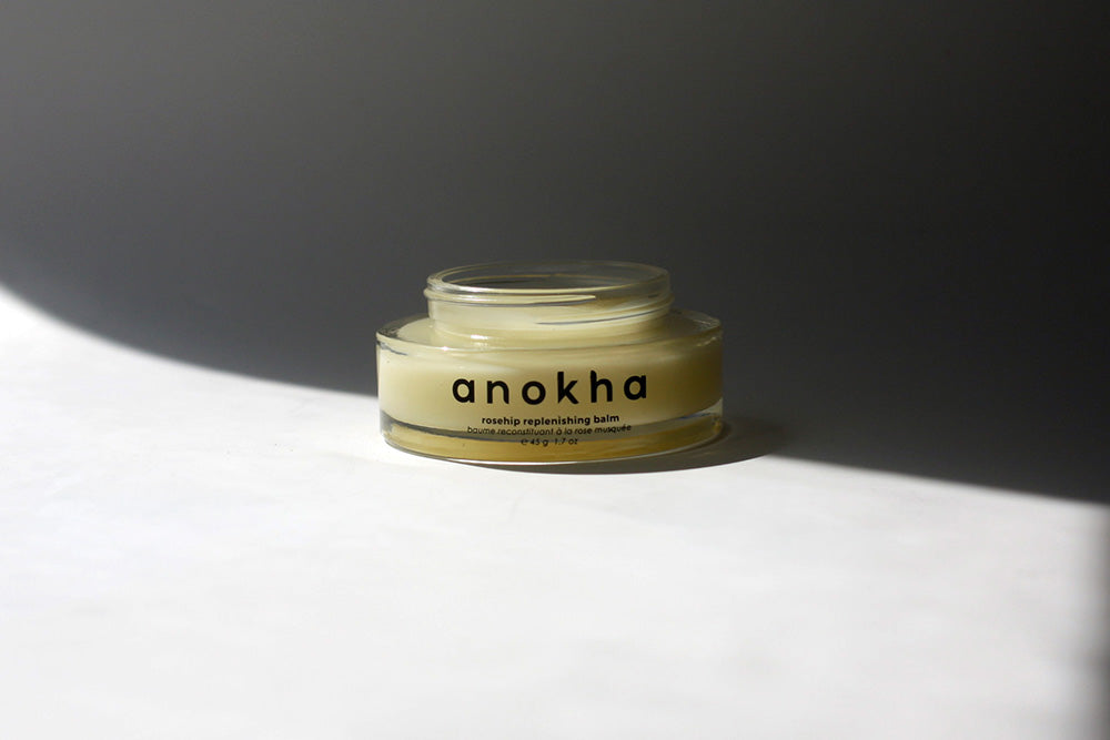 Anokha rejuvenating balm in a clear glass, set against a dark gray background with a bright white foreground and dramatic side lighting.
