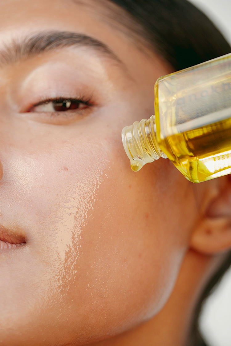 anokha rice bran & pomegranate facial oil bottle on face of young woman