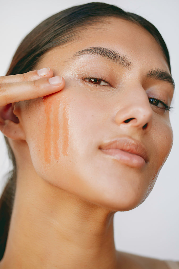 young woman applying anokha skincare bakuchiol & pomegranate facial oil to right cheek in three lines